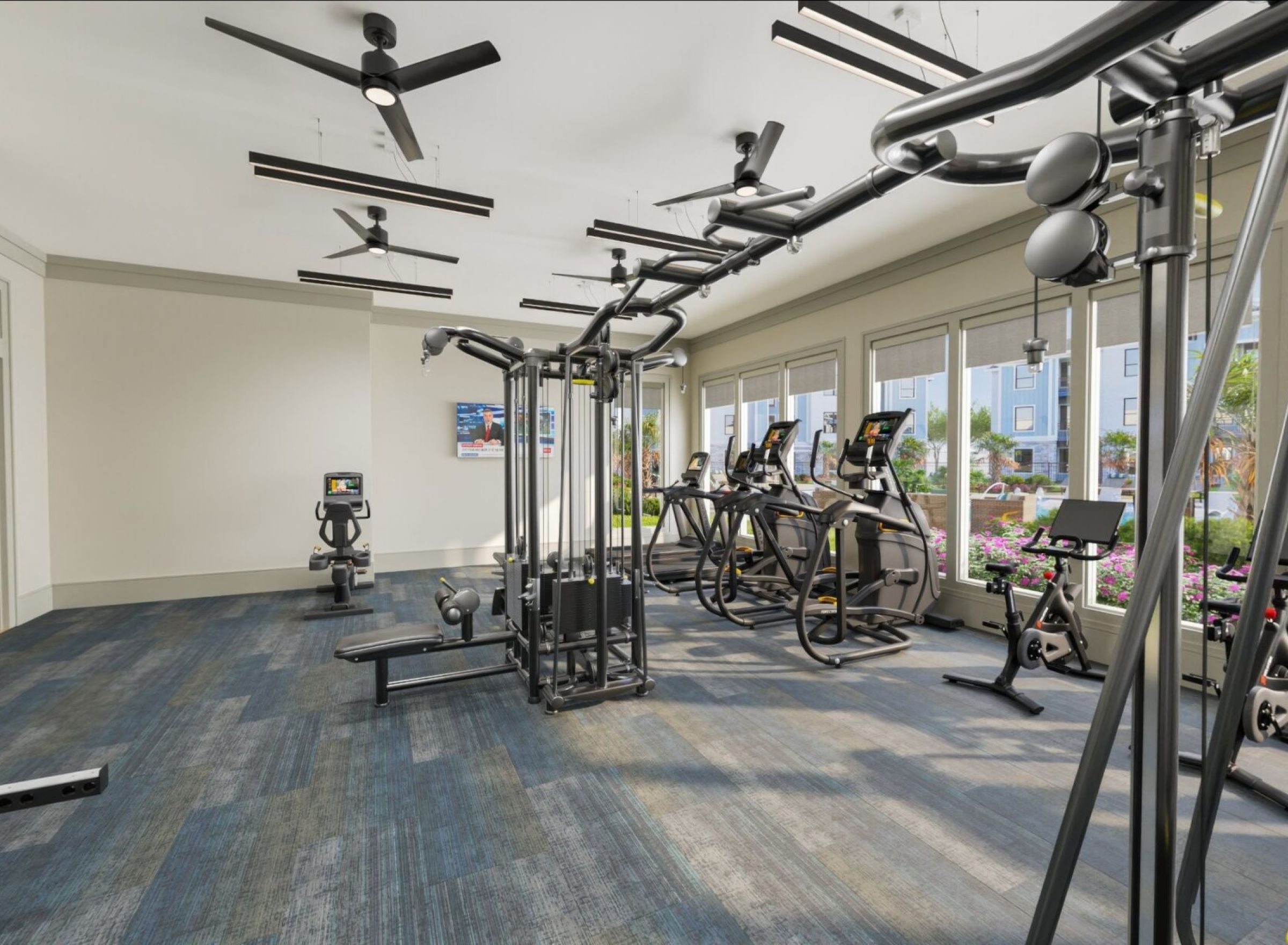 Modern gym with cardio machines, weight racks, and large windows letting in natural light.