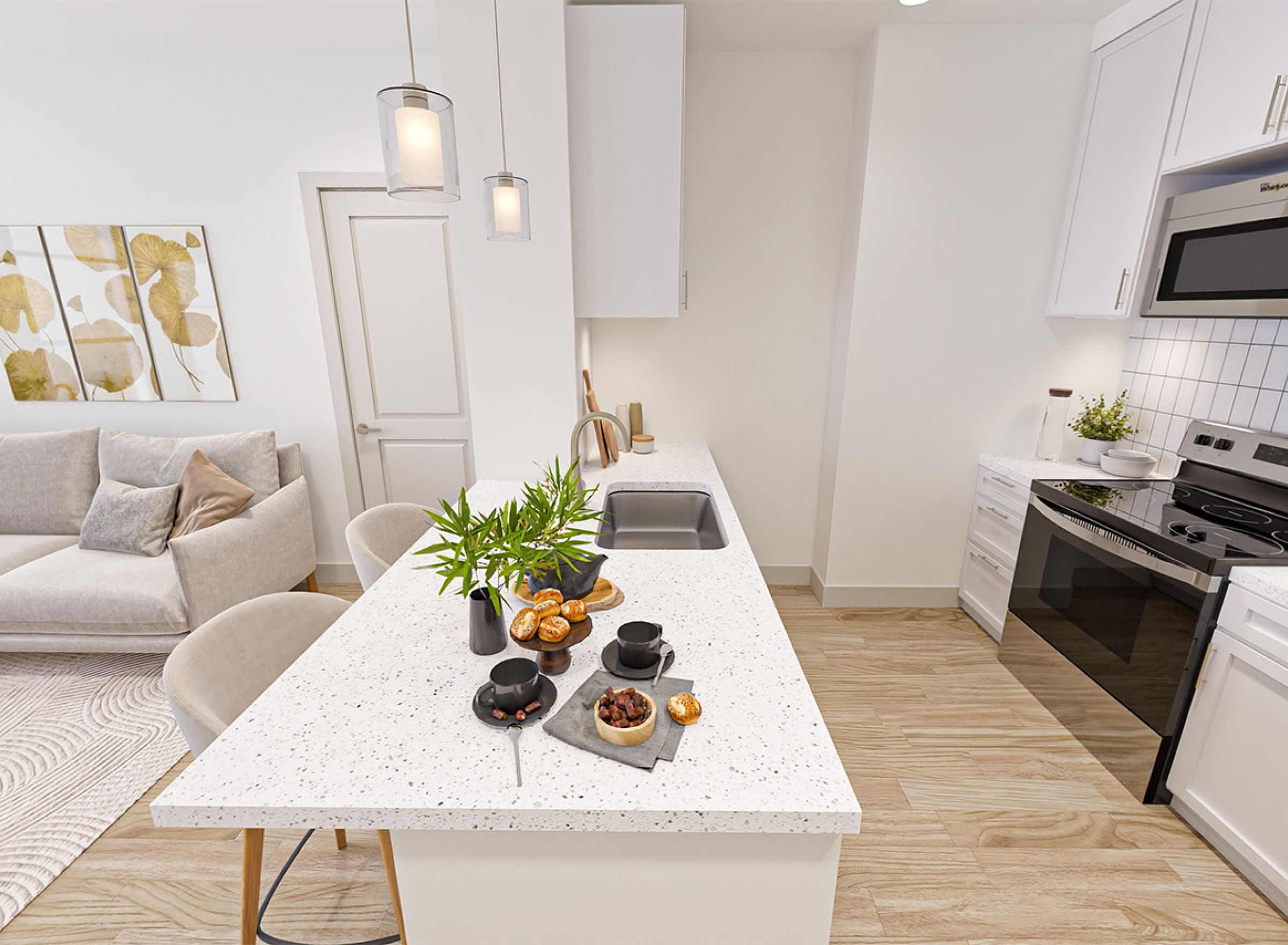 Monteverde Apartments Modern kitchen with white cabinets, island, and a small living area with a beige couch and wall art in the background.